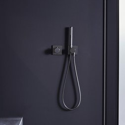 Der Duschbereich zeigt eine stilvolle, graue Fliesenwand mit einem schlichten, schwarzen Duschschlauch und einem Handgriff.
